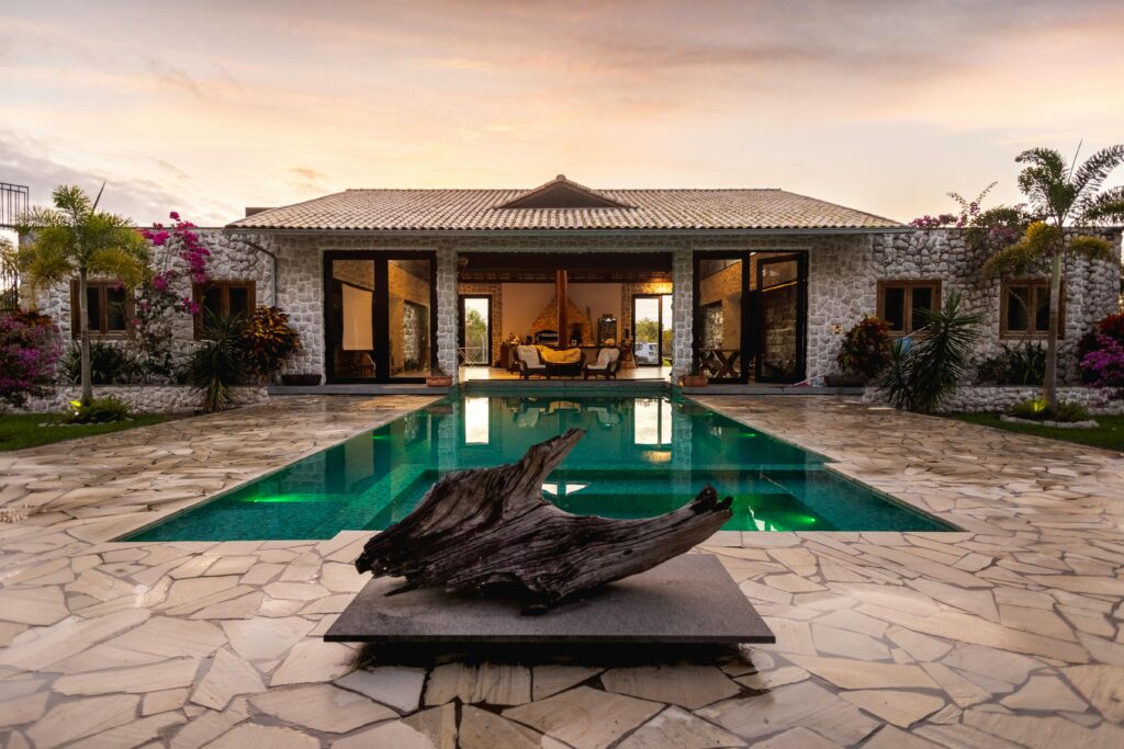 Elegant villa with a pool, stone facade, and tropical garden at sunset.